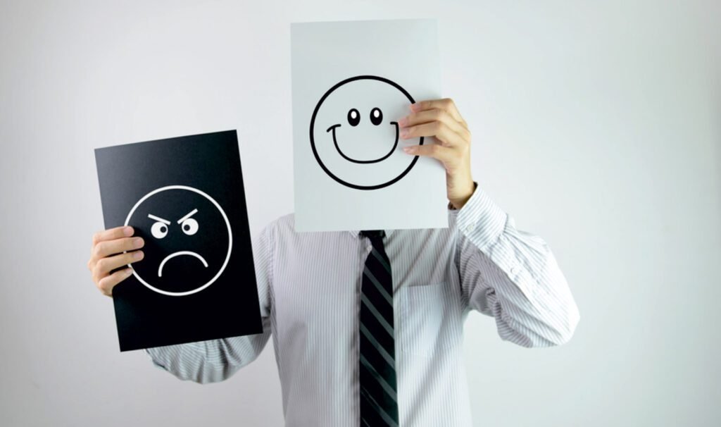 A person holding up a sad face and a happy face drawing