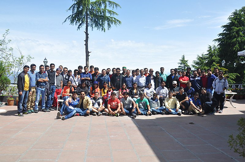 A large group gathers on a hillside lawn for a photograph.
