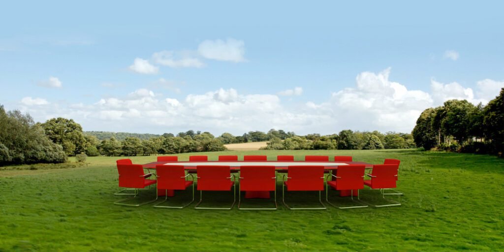 A long conference table with red chairs set up in the middle of a green meadow