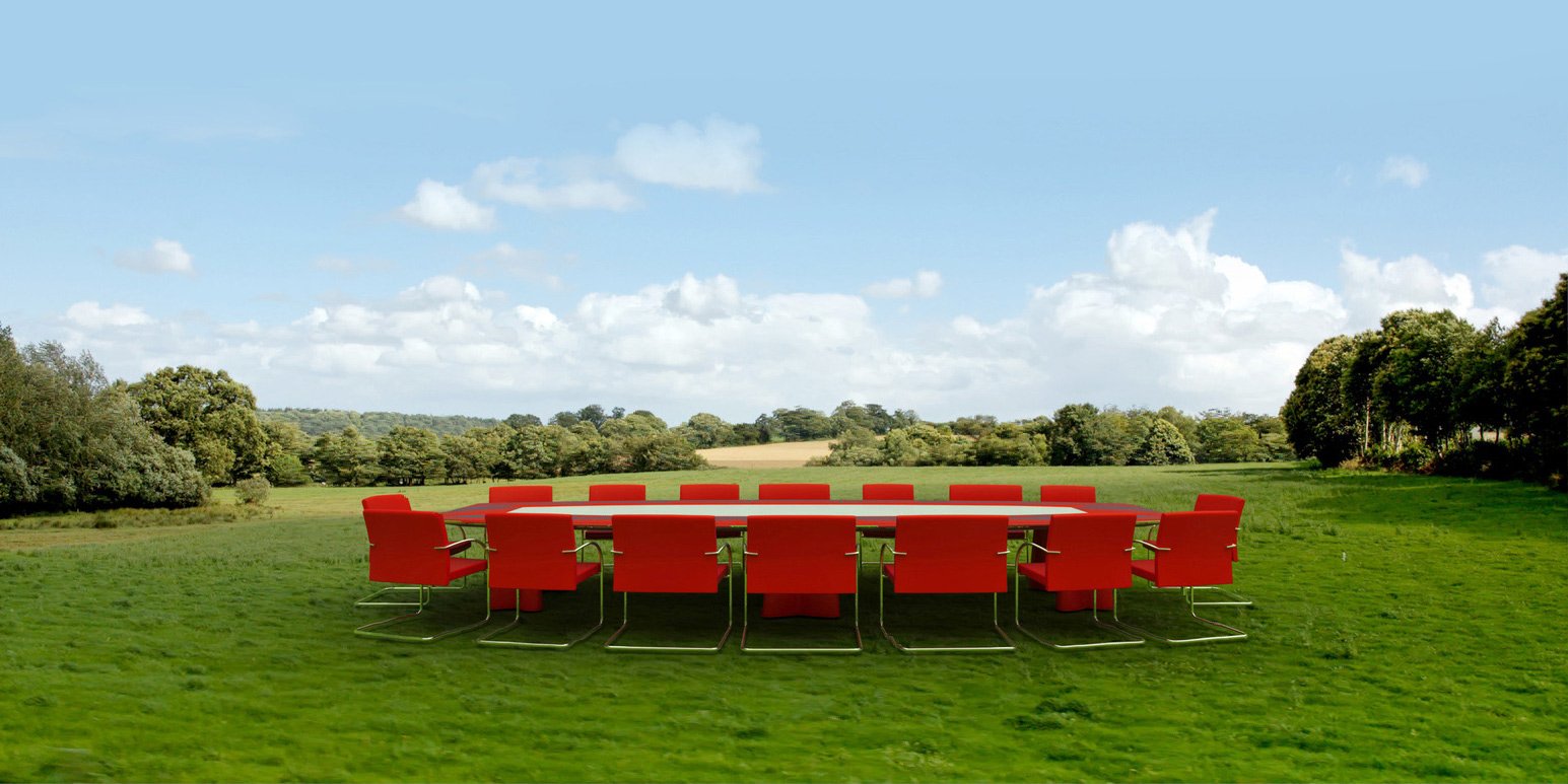 A long conference table with red chairs set up in the middle of a green meadow