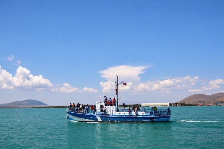 A passenger boat with guests on deck, crossing a turquoise lake under a blue sky.