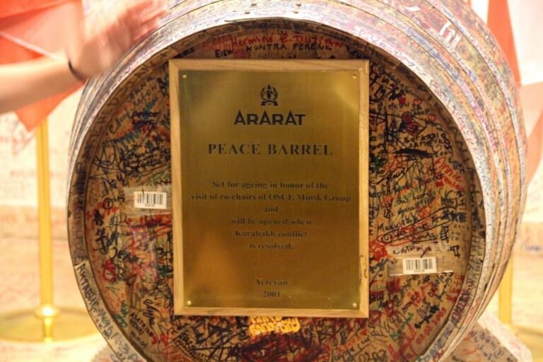 A brass plaque on a large wooden barrel covered in handwritten signatures.