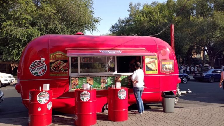 A red food truck on a city street, with a guest at the serving window.