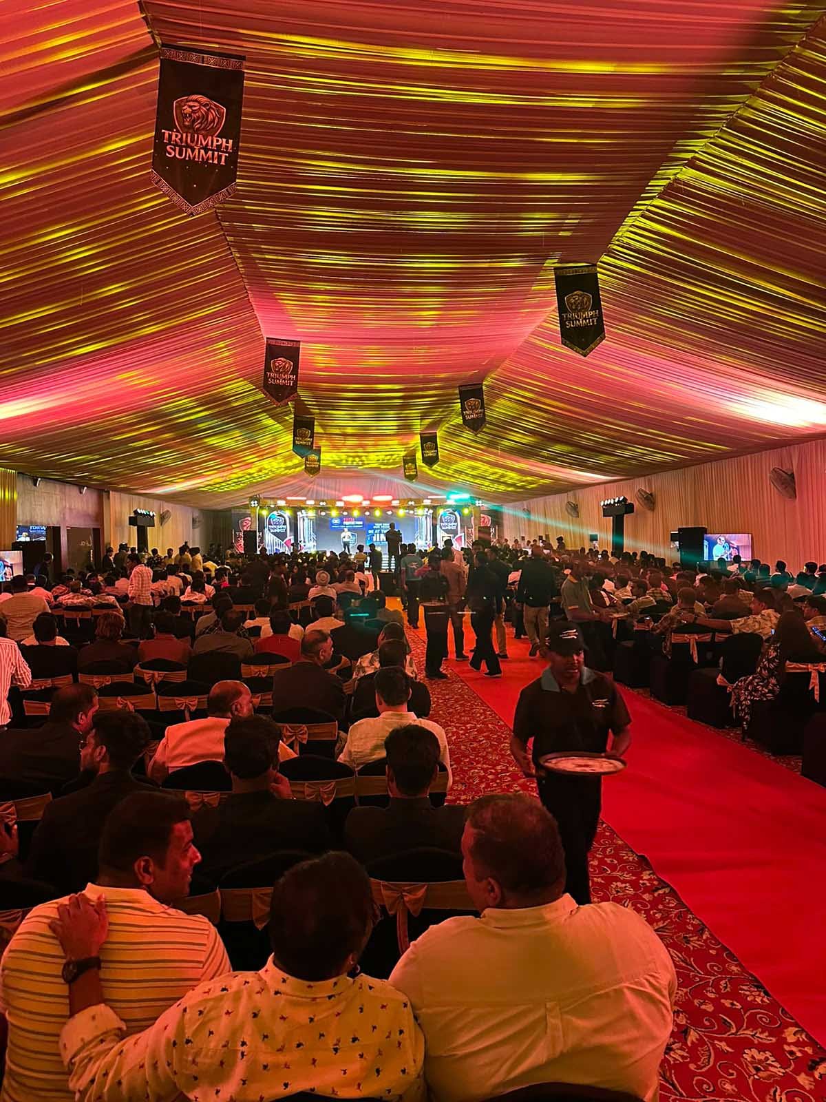 Guests seated in the Triumph Summit 2026 gala tent beneath a lit, draped ceiling with Triumph Summit banners